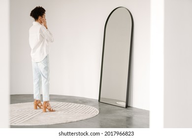 Young Black Woman Standing And Looking At Mirror Indoors