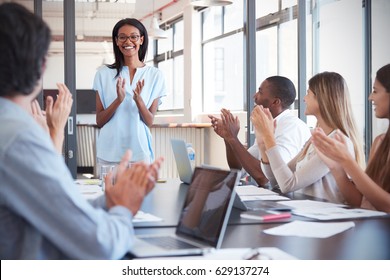 Young black woman stands clapping with colleagues at meeting - Shutterstock ID 629137274
