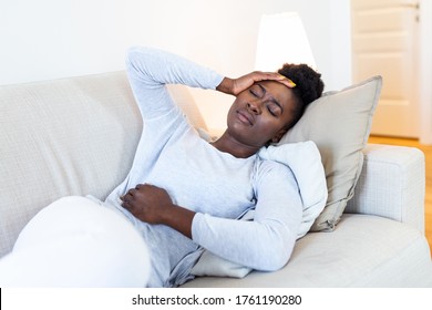 Young Black Woman Suffering From Stomachache On Sofa At Home. Woman Sitting On Bed And Having Stomach Ache. Young Woman Suffering From Abdominal Pain While Sitting On Sofa At Home