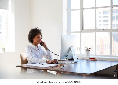 Young Black Woman Talking On Phone At Her Desk In An Office