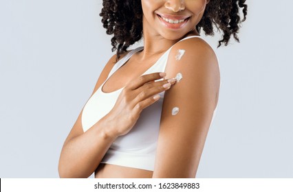 Young black woman using cream after shower for body care, skin care products concept, cropped