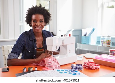 Young black woman using a sewing machine looking to camera