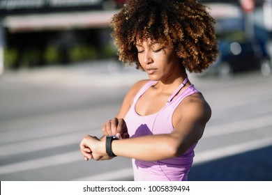 Young Black Woman Using Smartwatch Touching Touchscreen In Active Sports Activity. Girl With Afro Hair Looking At Her Smart Watch Screen.