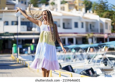 Junge schwarze Frau, die einen Seehafen entlang geht und ein schönes Sommerkleid trägt.