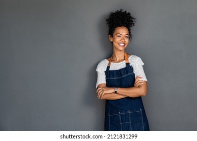 Young black woman wearing apron isolated on grey background with copy space. Portrait of successful african american woman with crossed arms on gray wall. Smiling black waitress looking at camera.