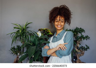 Young Black Woman Wearing Beige Apron Isolated On Grey Background With Copy Space. Portrait Of Successful African American Woman With Plants. Smiling Black Florist Looking At Camera.