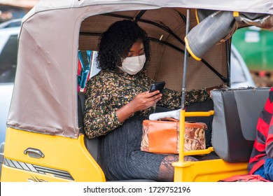 Young Black Woman Wearing Face Mask For Protection And Using Her Phone In Tuk Tuk Public Transport - Concept On Millennial Lifestyle After Lockdown, Connecting With People Through Smartphone 