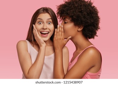 Young Black Woman Whispers Secret To Her Caucasian Friend, Gossip Together And Spread Rumours. Emotional European Girl Feels Amazed To Hear Confidential Information From Companion. Secrecy, Gossiping