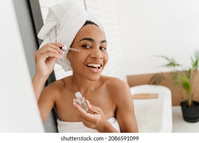 Young Black Woman Wrapped In Towels Applying Face Serum At Bathroom