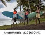 Young black women surfers walking with their surfboards and going to surf class by the beach in Sao Tome and Principe, Africa