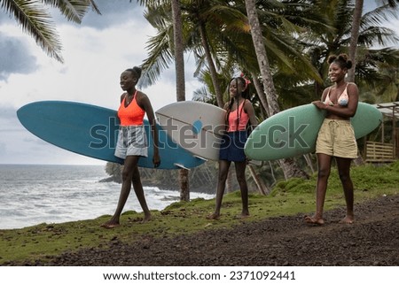 Young black women surfers walking with their surfboards and going to surf class by the beach in Sao Tome and Principe, Africa