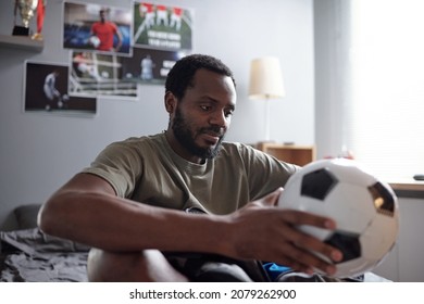 Young blackman in grey t-shirt looking at soccer ball in his hands while thinking of forthcoming play or championship