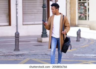 Young blackman looking at his smartphone while walking down the street.