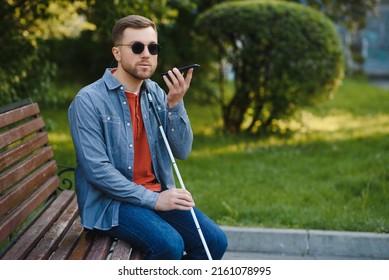 Young blind man with smartphone sitting on bench in park in city, calling - Powered by Shutterstock