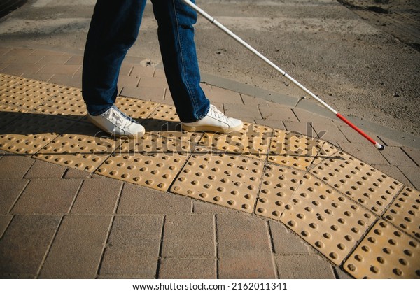 young blind man with white cane walking across the\
street in city.