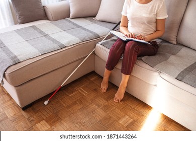 Young Blind Woman Reading Book Written In Braille At Home With White Cane . Blind Person Reading Book Written In Braille. Young Blind Woman Reading A Braille Book While Studying And Sitting At Home