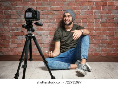 Young blogger with recording video against brick wall background