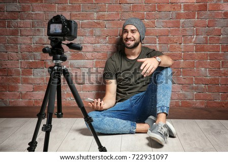 Young blogger with recording video against brick wall background