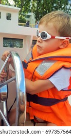 A young blond boy navigating on a small motor boat