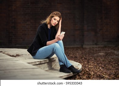 Young Blond Business Woman Using Smart Phone On City Street Stylish Fashion Model In Black Jacket And Blue Jeans Outdoor