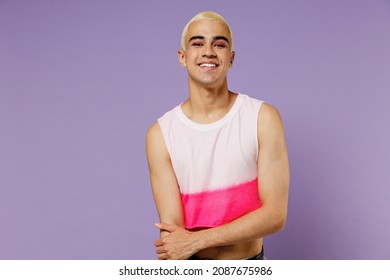 Young blond cool fun latin gay man 20s with make up wearing fashionable bright pink top look camera isolated on plain pastel purple background studio portrait. People lifestyle fashion lgbtq concept