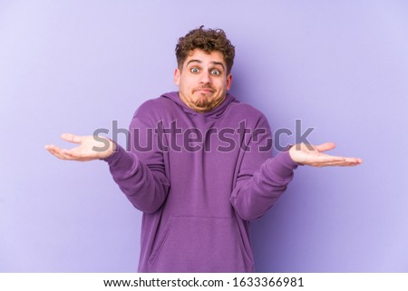 Young blond curly hair caucasian man isolated doubting and shrugging shoulders in questioning gesture.