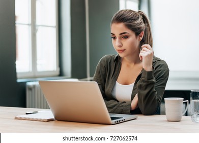 Young blond female student working on a laptop concentrating on reading the screen. - Shutterstock ID 727062574