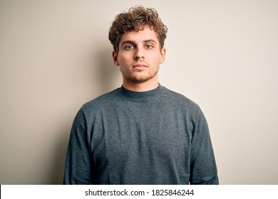 Young blond handsome man with curly hair wearing casual sweater over white background with serious expression on face. Simple and natural looking at the camera. - Powered by Shutterstock