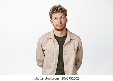 Young Blond Handsome Man Looking Bored, Roll Eyes Up And Exhale, Standing With Hands Behind Back Against White Background