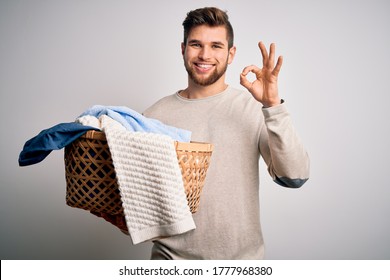 Young blond man with beard and blue eyes doing chores holding wicker basket with clothes doing ok sign with fingers, excellent symbol