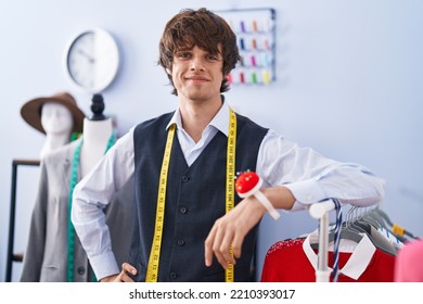 Young Blond Man Tailor Smiling Confident Leaning On Clothes Rack At Clothing Factory