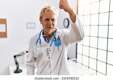 Young blond man wearing doctor uniform and stethoscope at clinic angry and mad raising fist frustrated and furious while shouting with anger. rage and aggressive concept.  - Shutterstock ID 2191930513