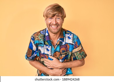 Young Blond Man Wearing Summer Shirt Smiling And Laughing Hard Out Loud Because Funny Crazy Joke With Hands On Body. 