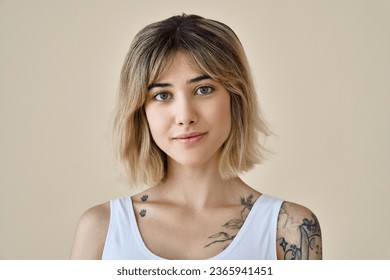 Young blond pretty smiling girl beauty female model with short blonde hair beautiful face healthy skin and tattoos looking at camera isolated at beige background. Close up headshot portrait.