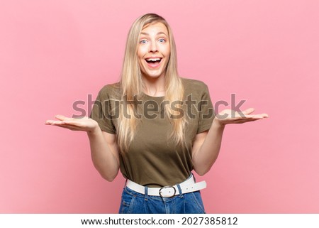 young blond pretty woman feeling happy, excited, surprised or shocked, smiling and astonished at something unbelievable