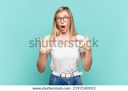 young blond pretty woman feeling happy, surprised and proud, pointing to self with an excited, amazed look