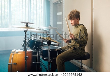 Young blond teen boy play drum kit in studio.