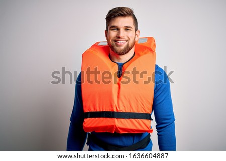 Young blond tourist man with beard and blue eyes wearing lifejacket over white background with a happy and cool smile on face. Lucky person.