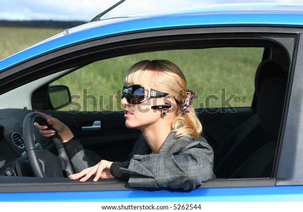 young blond woman in a blue car in sun-glasses\
with hands free headset