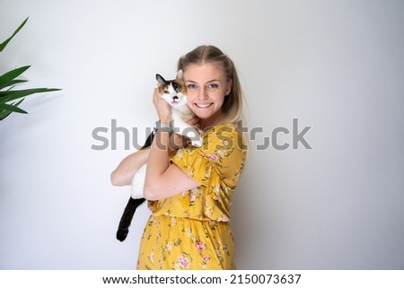 young blond woman carrying calico white cat on arms embracing the kitty smiling at camera looking happy with copy space