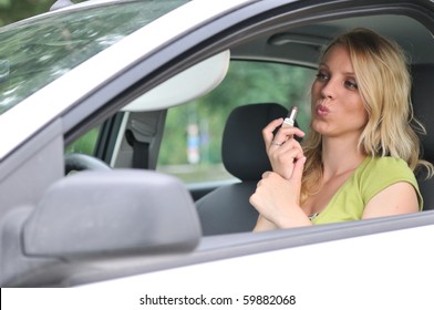Young blond woman doing makeup with lipstick in car