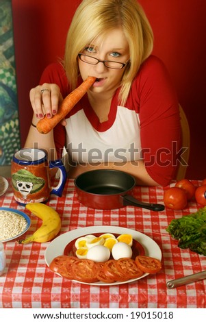 young blond woman eating a carrot and seating at a table