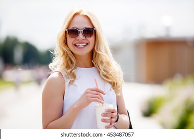 Young Blond Woman Holding Milkshake With Straw And Looking At Camera