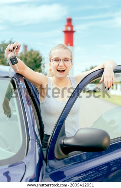 Young blond woman outside a car with a\
lighthouse as background