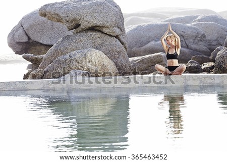Young blond woman performing yoga pose by pond