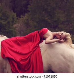 young blond woman in red lying on a horse