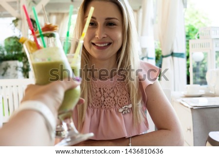 young blond woman sit in the cafe with friend and drink green healthy smoothiie , wearing pink dress