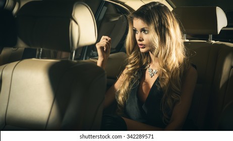 Young Blond Woman Sitting On A Backseat Of A Luxury Car At Night 