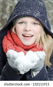 Young Blond Woman Smiles With Beanie And Scarf Blows In A Handful Of Snow