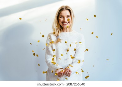 Young blond woman in white cozy sweater under confetti at home, People, holidays, celebrating, party, emotion and glamour concept.